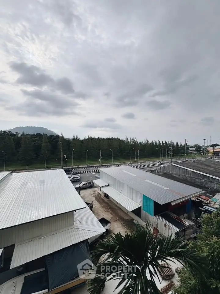 Scenic view of industrial buildings with lush greenery and cloudy sky backdrop.