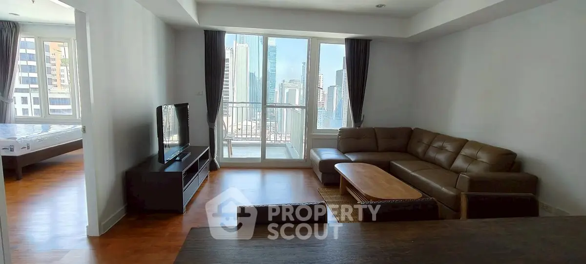 Spacious living room with modern furniture and city view balcony in high-rise apartment.