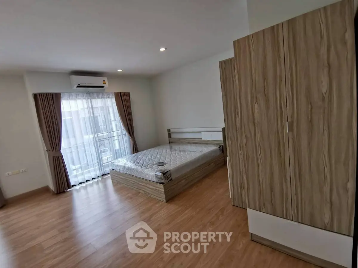 Spacious bedroom with wooden flooring and large window for natural light.