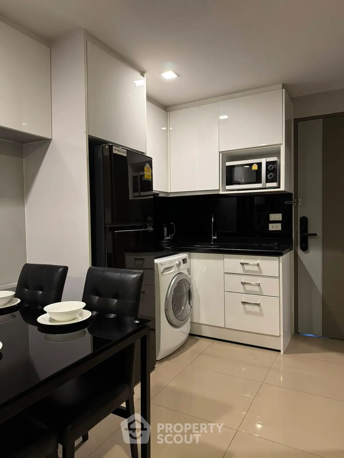 Modern kitchen with sleek black and white design, featuring appliances and dining area.