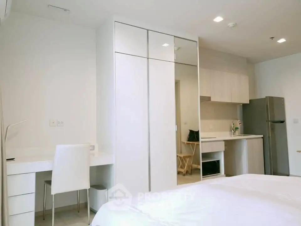 Modern bedroom with sleek white furniture and compact kitchen area, perfect for urban living.