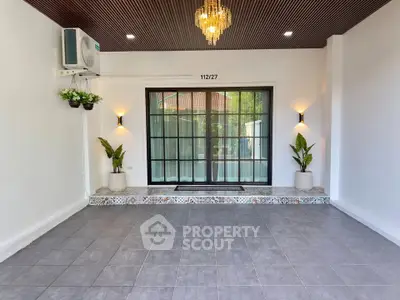 Spacious modern living room with elegant chandelier and large glass doors opening to a serene view.