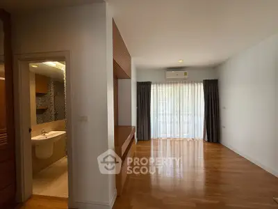 Spacious living room with wooden flooring and natural light, adjacent to a modern bathroom.