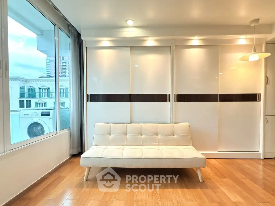 Modern living room with sleek white furniture and large windows offering city views.