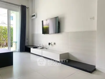 Modern living room with wall-mounted TV and sleek storage unit, featuring large windows and natural light.