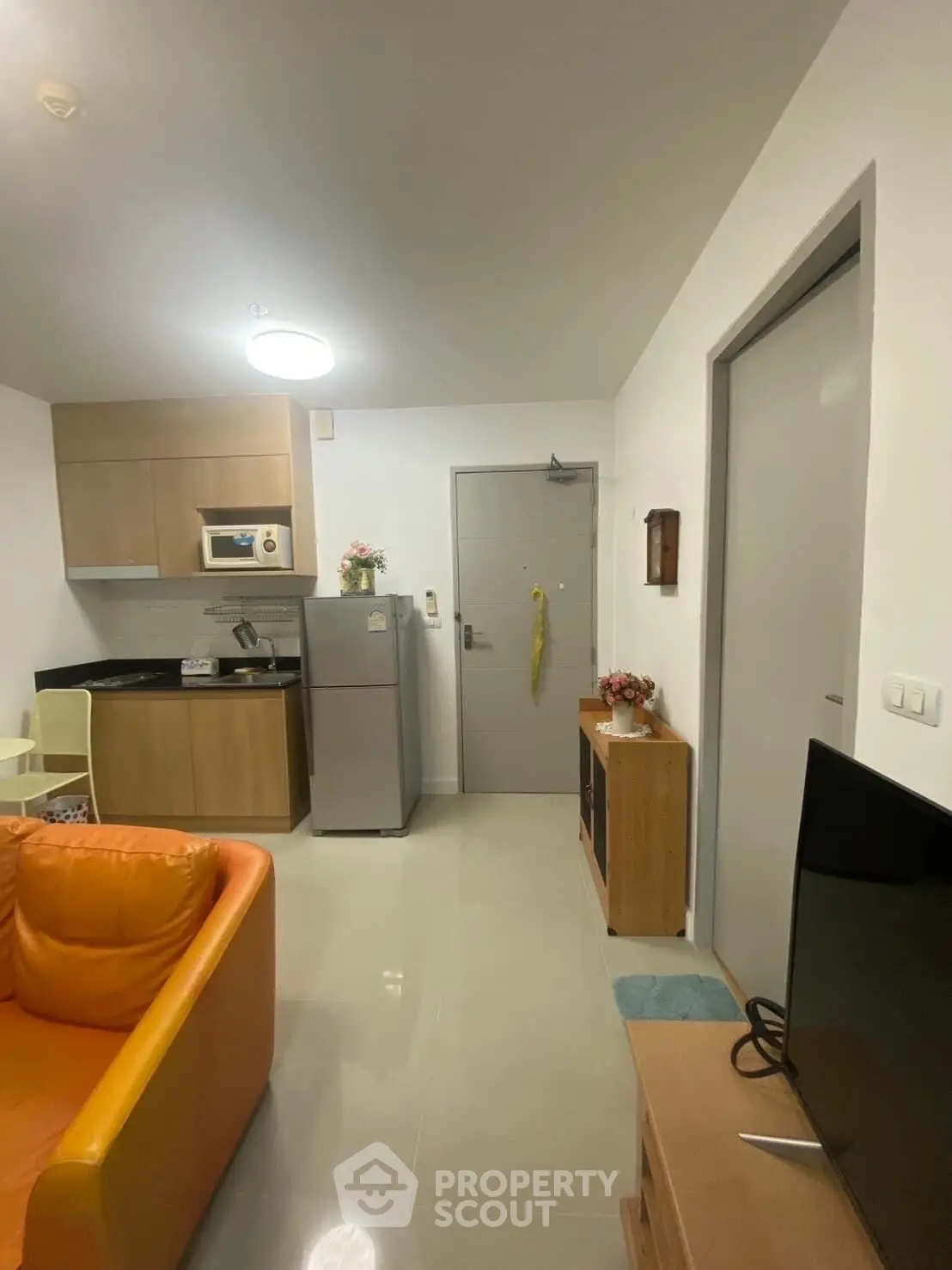 Modern compact living room with open kitchen and cozy orange sofa in a stylish apartment.