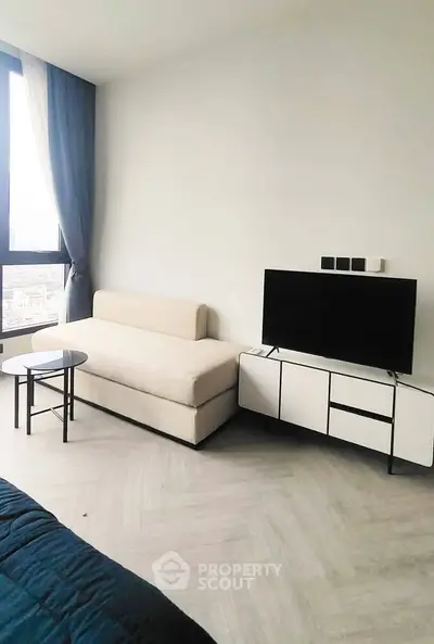 Modern living room with sleek furniture and large window offering city views.