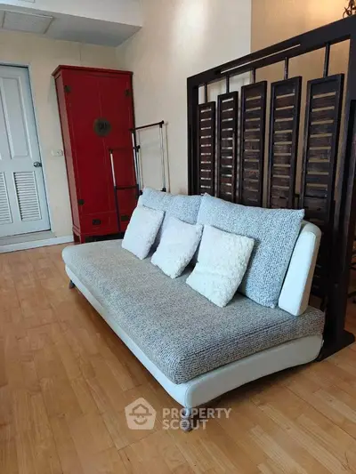 Stylish living room with modern sofa and wooden flooring, featuring a red cabinet and decorative partition.