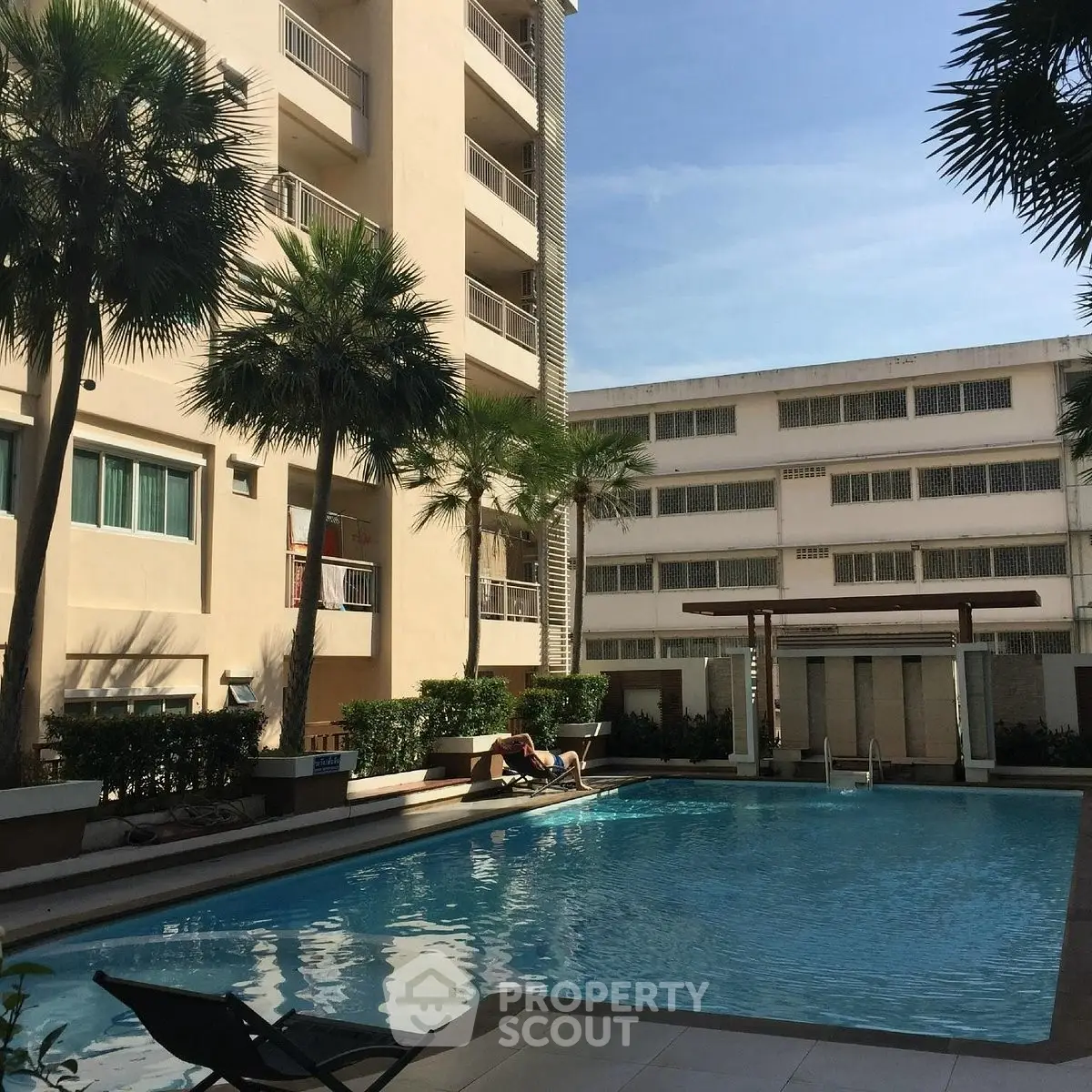 Luxurious apartment complex with inviting swimming pool and palm trees under clear blue sky.