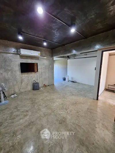 Modern industrial-style living room with concrete floors and exposed ceiling lights.