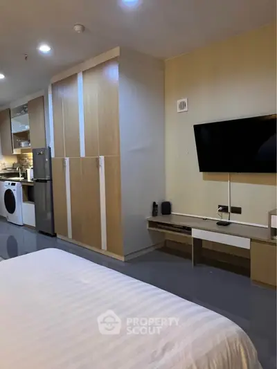 Modern studio apartment with sleek kitchen and cozy living area, featuring a wall-mounted TV and ample storage.