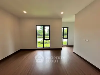 Spacious empty room with large windows and wooden flooring, ideal for customization.