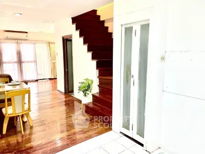 Spacious living area with wooden staircase and dining set, featuring natural light and elegant decor.