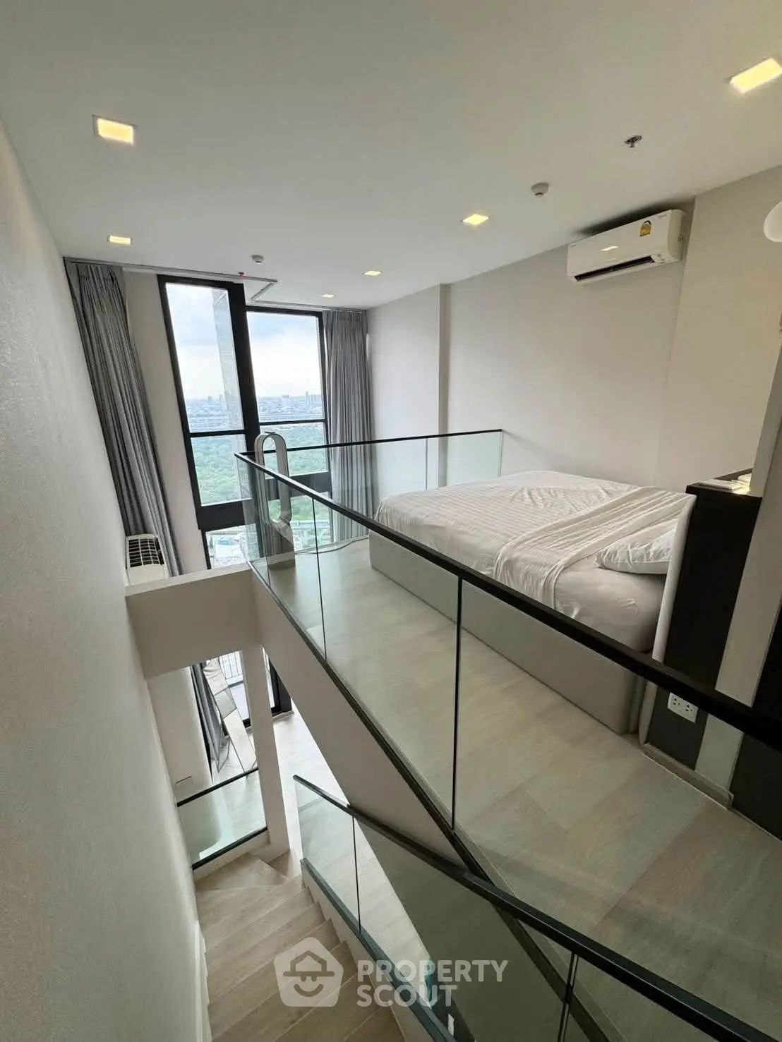 Modern loft bedroom with glass railing and large windows offering stunning views.