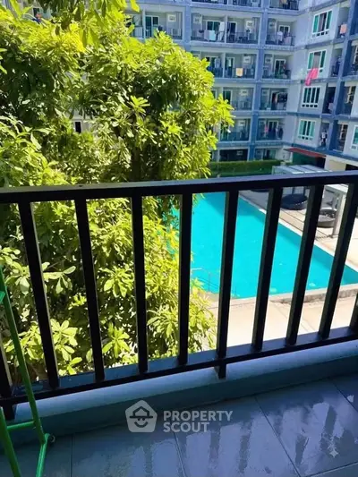 Charming balcony view overlooking a lush garden and inviting pool in a modern apartment complex.