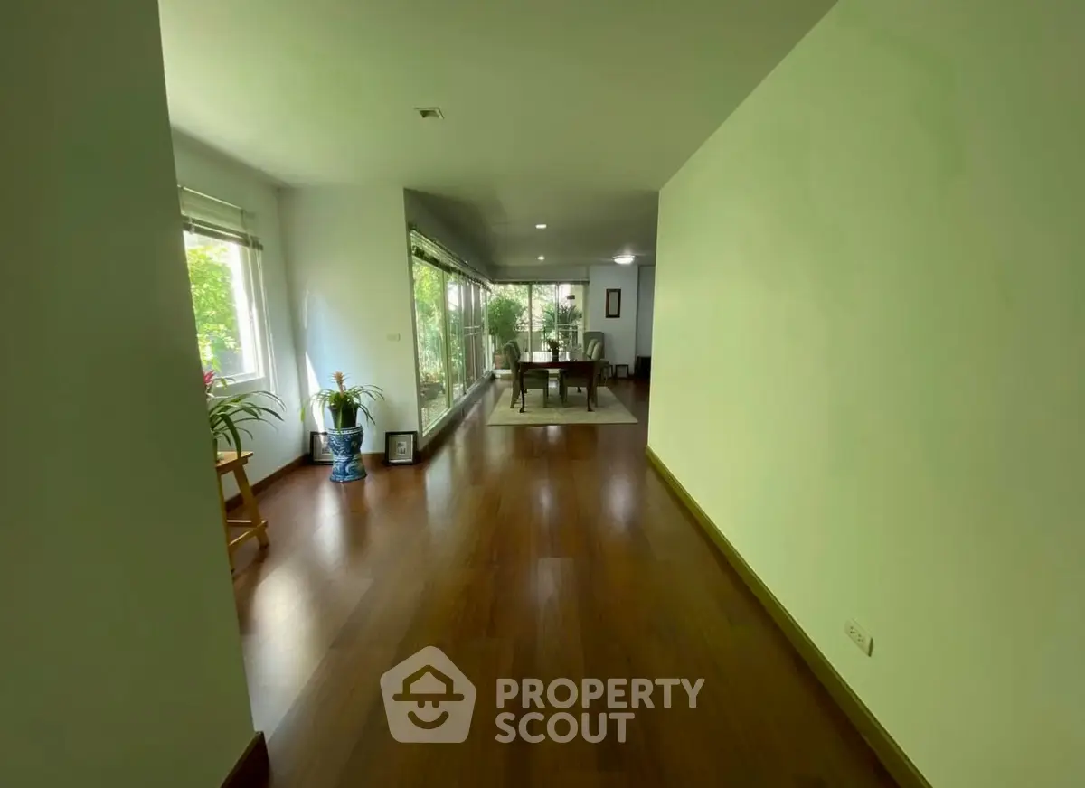 Spacious living room with wooden flooring and large windows offering natural light and garden view.