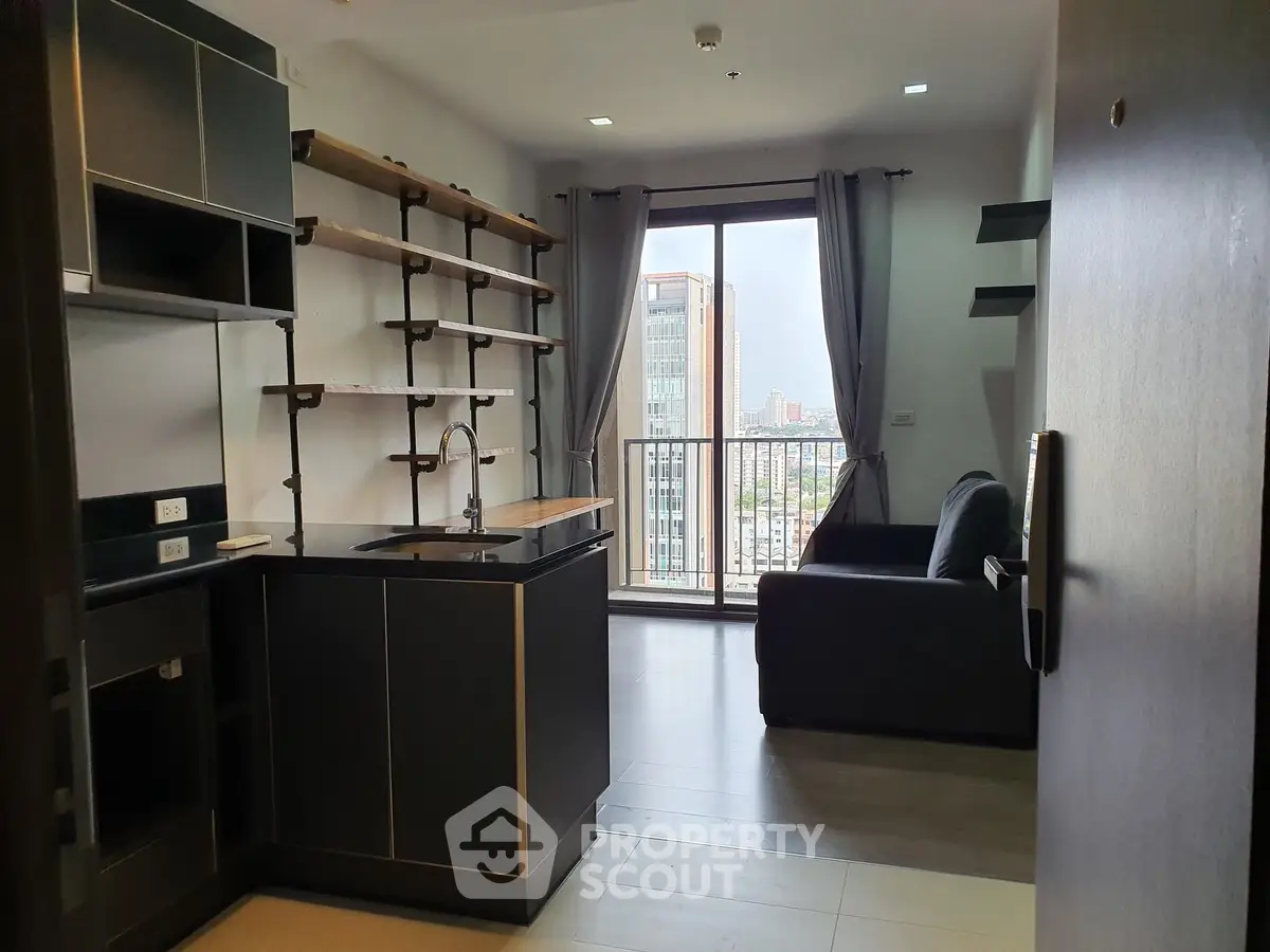 Modern studio apartment with sleek open kitchen layout, ample shelving, and a cozy living space leading to a sunlit balcony with urban views.
