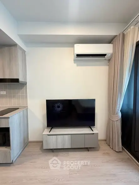 Modern living room with sleek TV setup and air conditioning, featuring stylish curtains and contemporary kitchen design.
