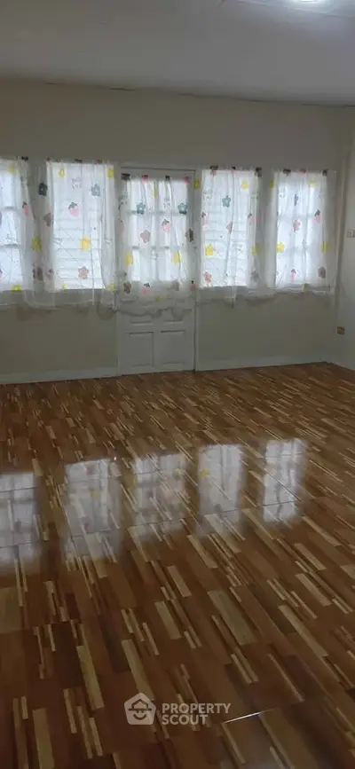 Spacious room with polished wooden floors and large windows with colorful curtains.