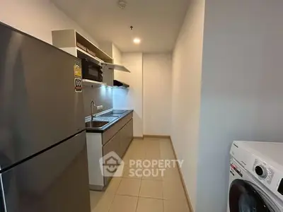 Modern kitchen with stainless steel appliances and washing machine in sleek apartment.