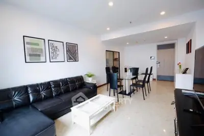Spacious modern living room with sleek black sofa and elegant dining area in open layout.