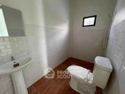 Modern bathroom with sleek white tiles and wooden floor, featuring a pedestal sink and toilet.