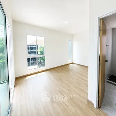 Spacious empty room with wooden flooring and large windows offering natural light.