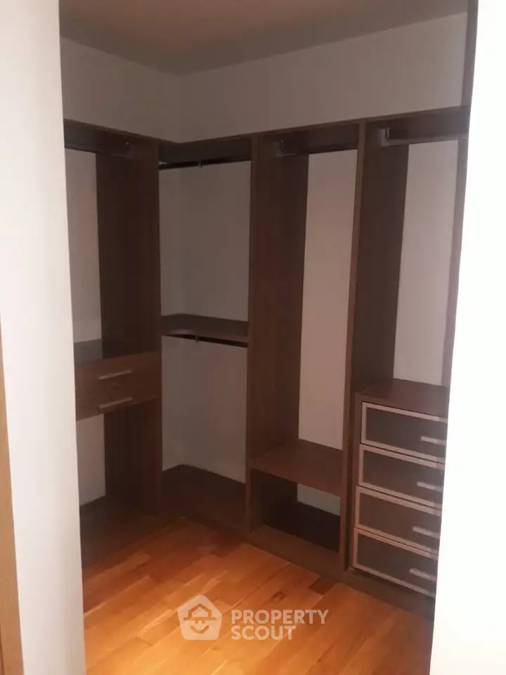 Spacious walk-in closet with wooden shelves and drawers, perfect for organized storage.