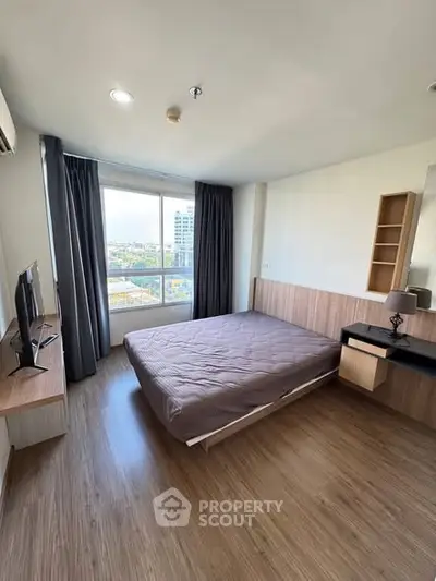 Spacious bedroom with large window and modern furnishings, offering a bright and inviting atmosphere.