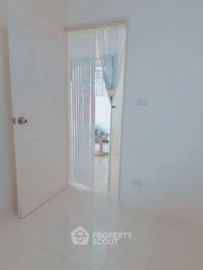 Bright minimalist room with open door leading to airy space, showcasing sleek tiled flooring.