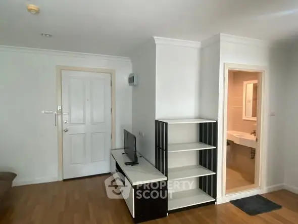 Modern apartment interior with wooden flooring, TV unit, and open bathroom entrance.