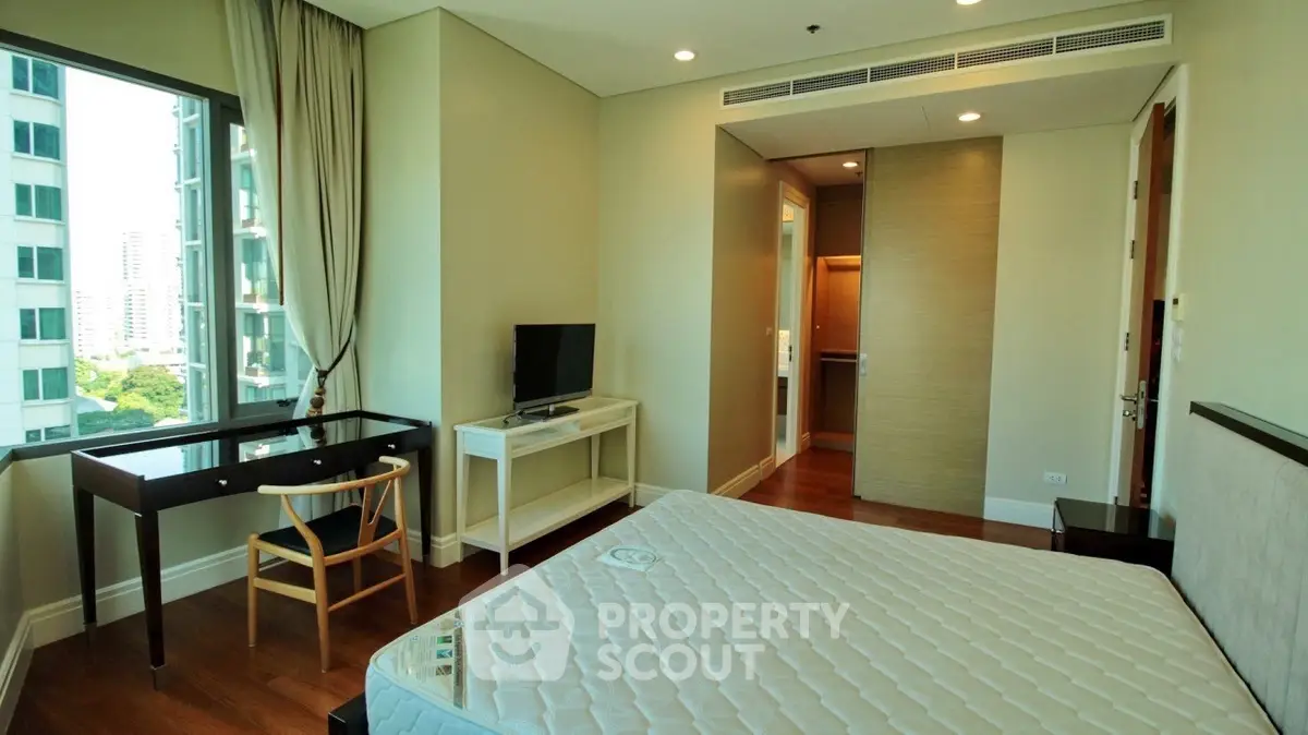 Spacious bedroom with large window and modern furnishings in high-rise apartment.