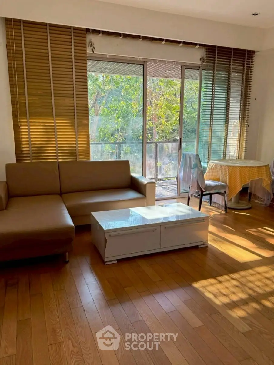 Spacious living room with large windows and balcony access, featuring modern furniture and natural light.