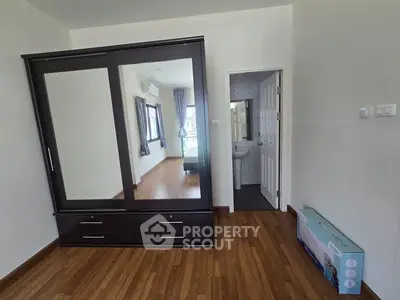 Spacious bedroom with wooden flooring and large wardrobe, featuring a glimpse into an adjoining bathroom.