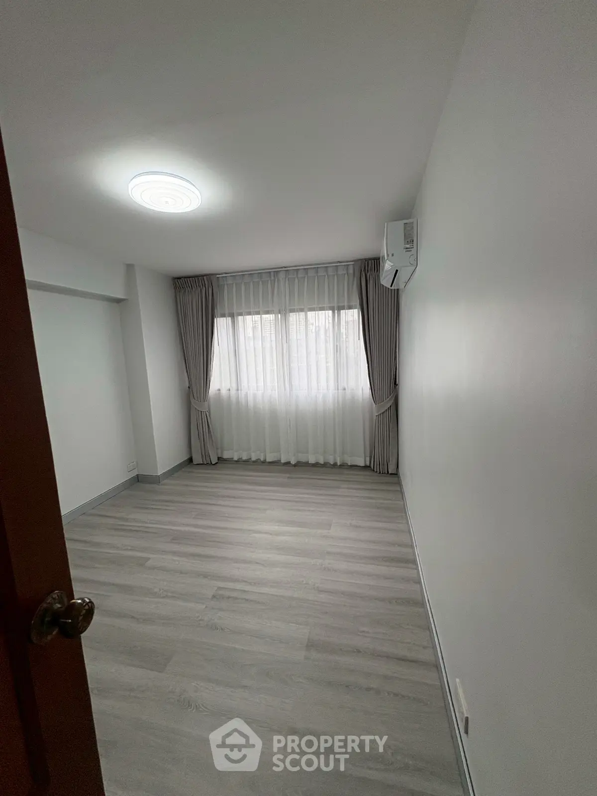 Spacious empty room with large window and modern flooring, perfect for customization.