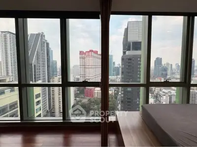 Stunning city view from modern high-rise apartment bedroom with floor-to-ceiling windows.