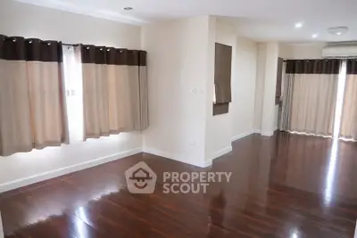 Spacious empty living room with polished wooden floors and large windows.
