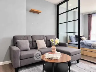 Modern living room with stylish gray sofa and glass partition leading to bedroom
