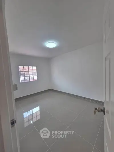 Spacious empty room with glossy tiled floor and bright window, perfect for customization.