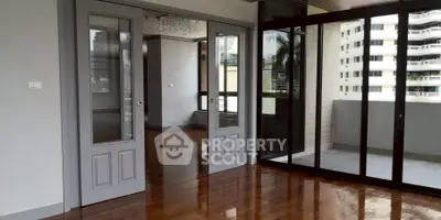 Spacious modern living room with glass doors leading to a balcony, featuring polished wooden floors.