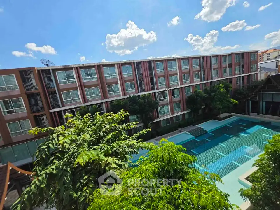 Modern apartment complex with pool and lush greenery under a bright blue sky.