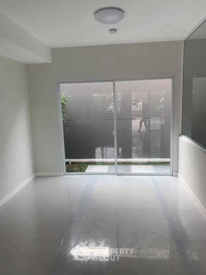 Spacious empty room with large sliding glass doors leading to a small garden area, perfect for natural light.