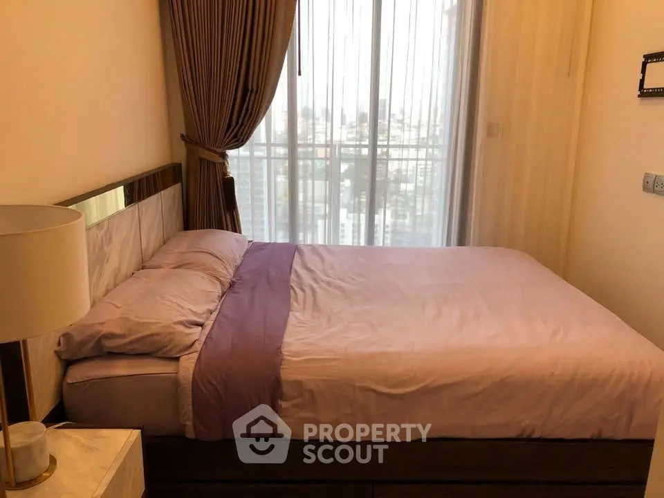 Cozy bedroom with large window and elegant curtains, offering a serene city view.