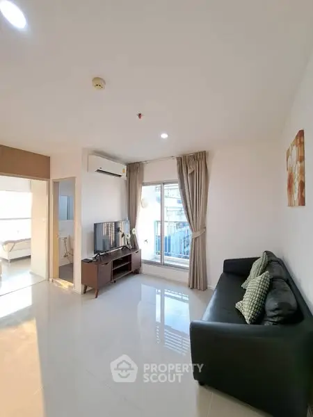 Modern living room with sleek sofa, TV, and balcony access in bright apartment.