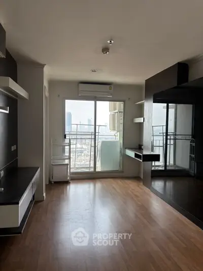 Spacious modern living room with balcony and city view, featuring sleek hardwood floors and built-in shelving.
