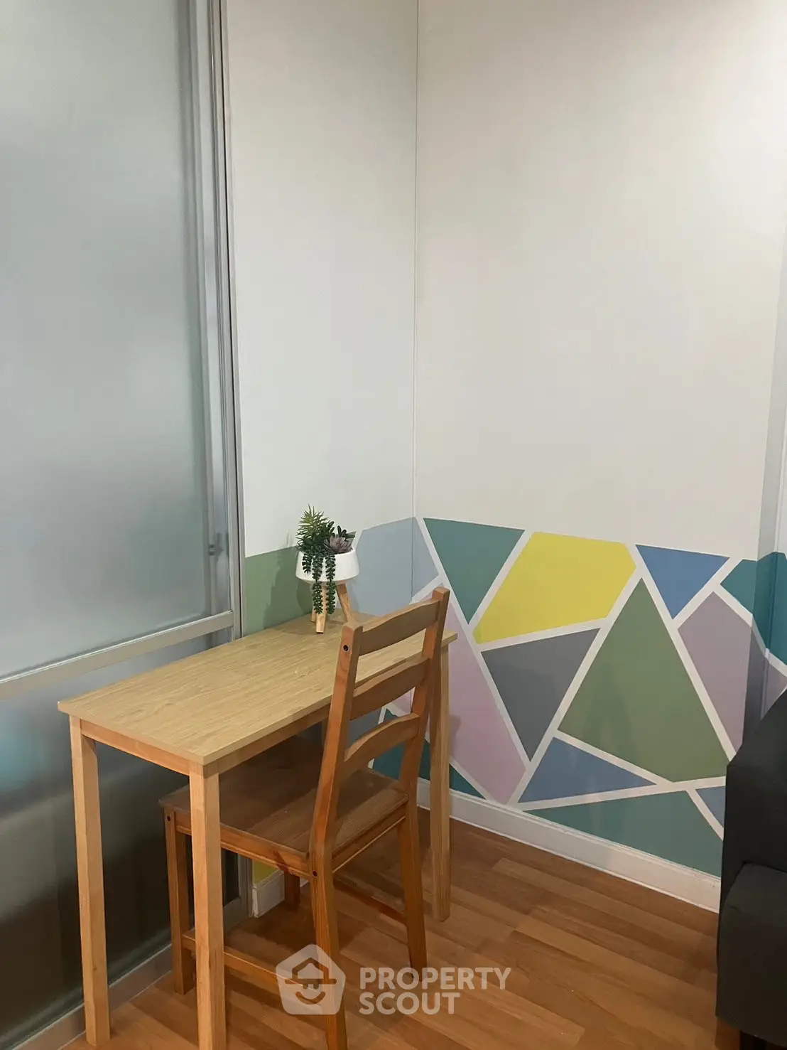 Cozy study nook with wooden desk and chair, colorful geometric wall design, and potted plant.