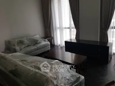 Spacious living room with wrapped furniture and elegant curtains, perfect for modern living.