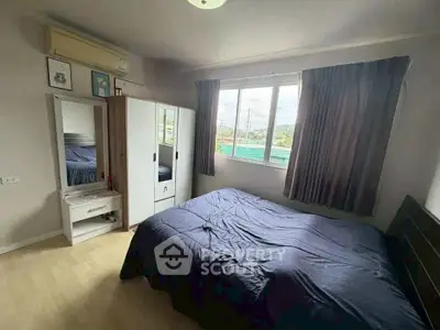 Cozy bedroom with large window and modern furnishings in a well-lit apartment.