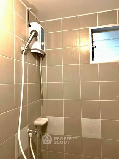 Compact bathroom with tiled walls and electric shower heater, ideal for efficient space use.