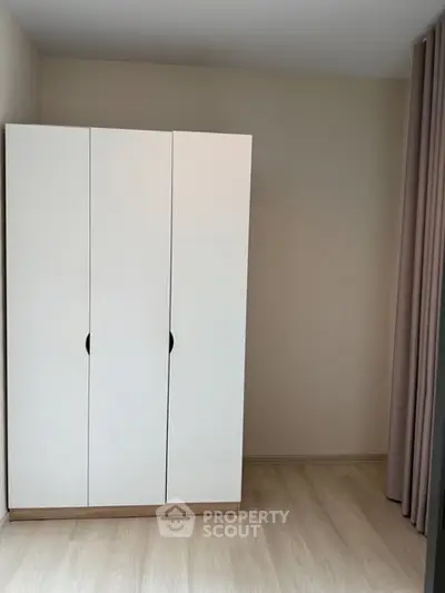 Minimalist bedroom with sleek white wardrobe and light wood flooring.